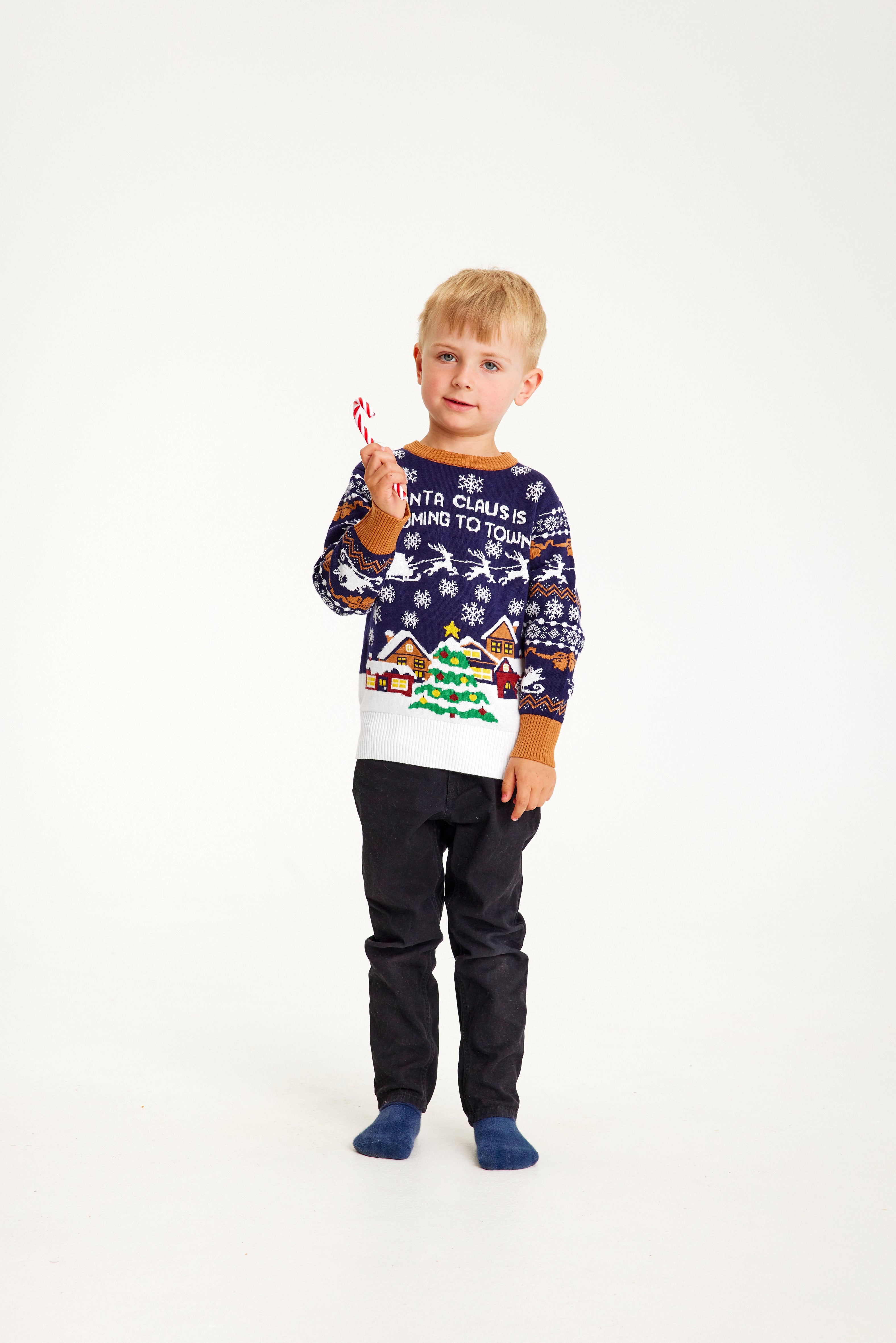 Et barn med en sukkerstok iført en blå julesweater.
